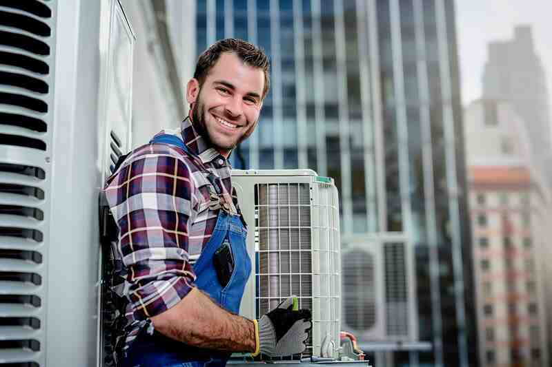 HVAC technician in plaid shirt and overalls servicing an air conditioning unit