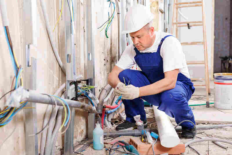 Experienced electrician laying electric wires in building under construction